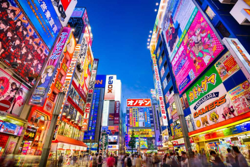   TOKYO, JEPUN - 1 OGOS 2015: Orang ramai lalu di bawah papan tanda berwarna-warni di Akihabara. Daerah elektronik bersejarah telah berkembang menjadi kawasan membeli-belah untuk permainan video, anime, manga dan barangan komputer.