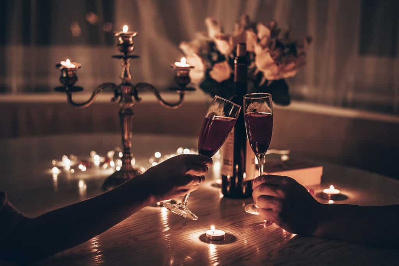   Käed, kus mees ja naine hoiavad veiniklaase ja õhtustavad kodus laua taga romantilist küünlavalgel. Mehe ja naise käed hoiavad klaasi veini. Valentini kontseptsioon's day or Candlelight date at night.